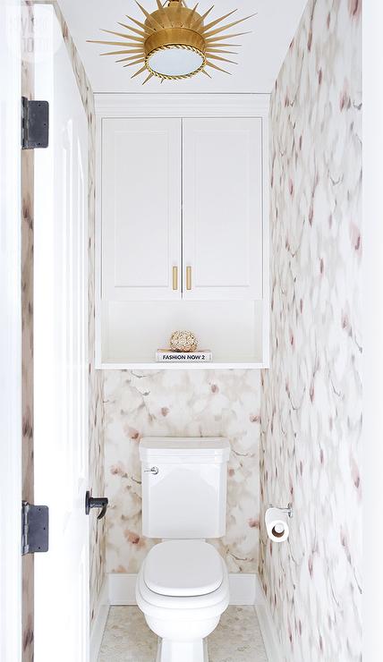 Chic water closet is clad in pink and gray floral wallpaper lined with  a cabinet and shelf hovering over a toilet illuminated by a Soleil Small  Pendant.