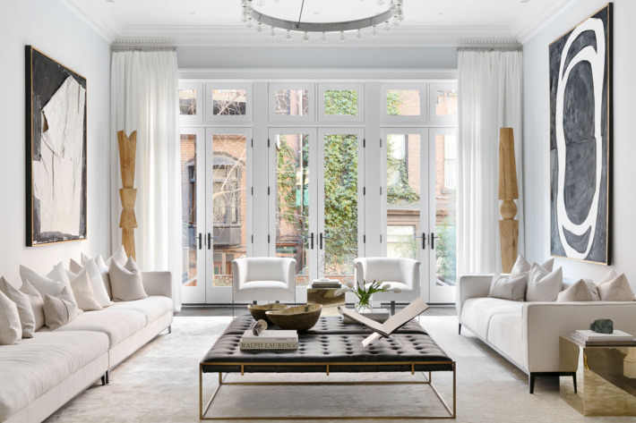 apartment with white walls, white couches, leather ottoman, and coffee  table book -