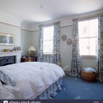 Blue carpet and floral patterned curtains in traditional bedroom with white  duvet on brass bed