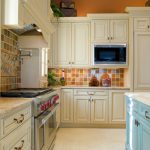 A country kitchen with a light blue island and multicolored ceramic tiles  for the backsplash.