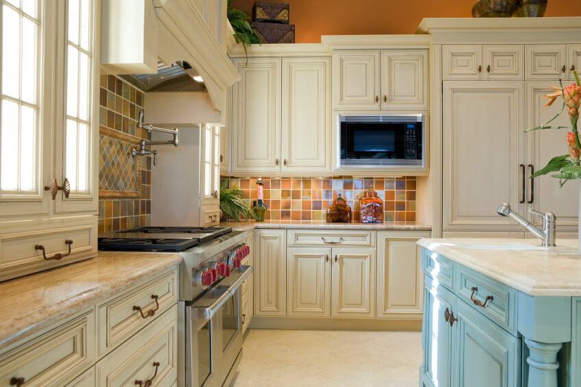 A country kitchen with a light blue island and multicolored ceramic tiles  for the backsplash.