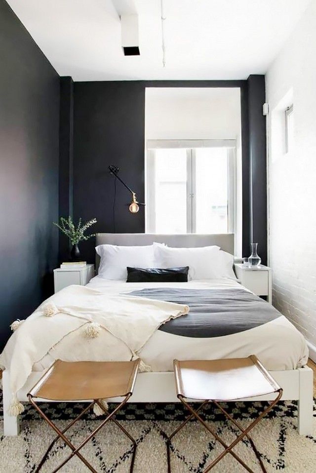 Small Swedish-inspired bedroom with black walls, simple bedding, and  leather stools